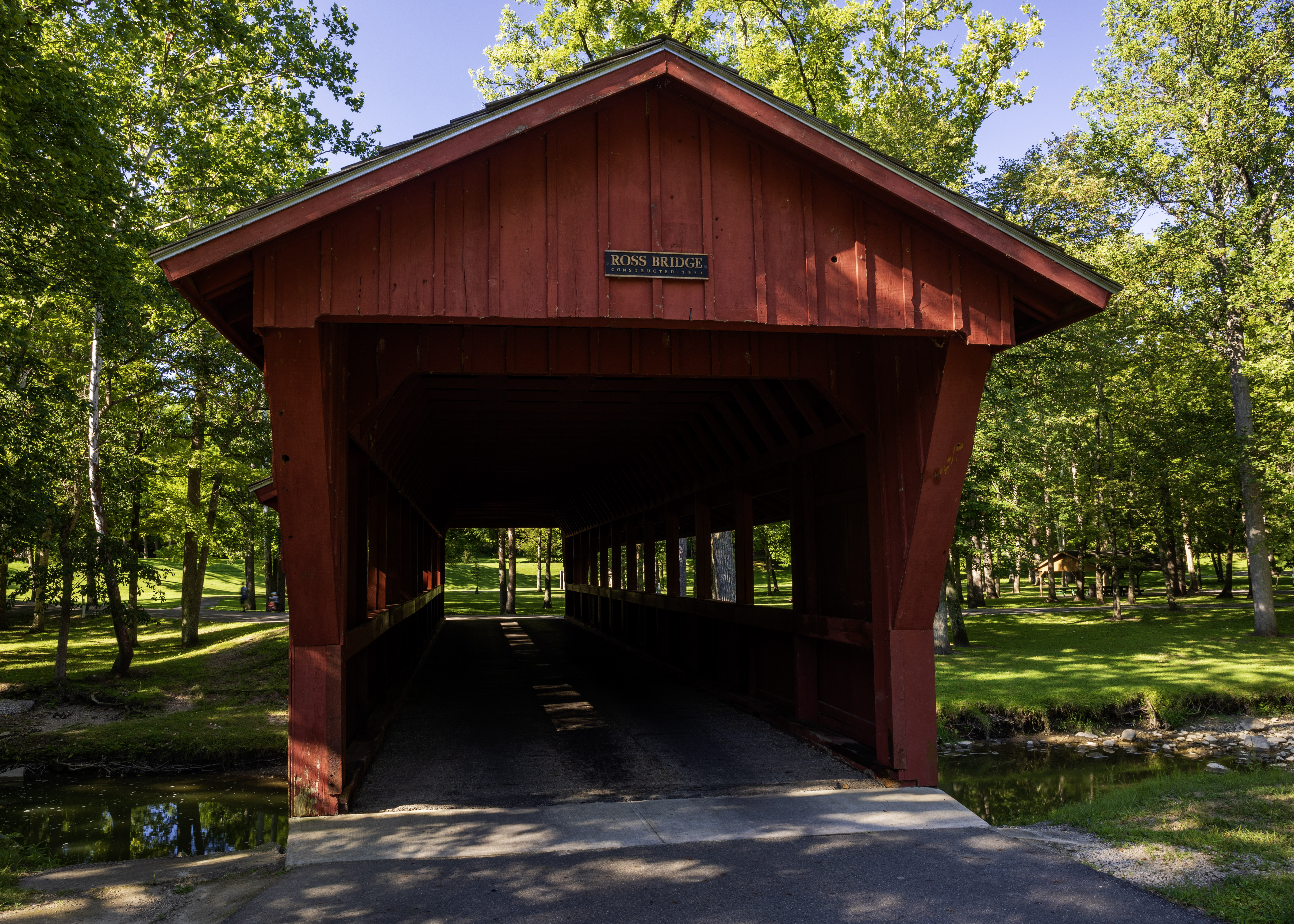 Front view of Ross Covered Bridge surrounded by green summer trees at Tawawa Park in Sidney Ohio
